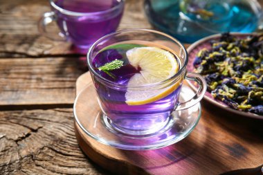 Bir bardak organik kelebek çayı, kurutulmuş çiçekler ve ahşap arka planda limon, yakın plan.