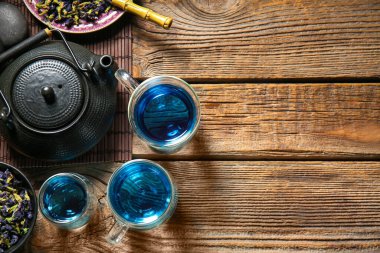 Bir bardak organik mavi çay ve ahşap zemin üzerinde kurumuş çiçekler.