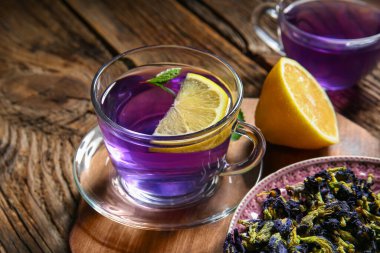 Bir bardak organik kelebek çayı, kurutulmuş çiçekler ve ahşap arka planda limon, yakın plan.