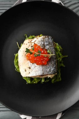 Gri ahşap zemin üzerinde deniz yosunu ve kırmızı havyar ile lezzetli levrek balığı tabağı