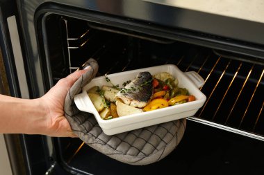 Mutfakta lezzetli levrek balığıyla fırından çıkan kadın.