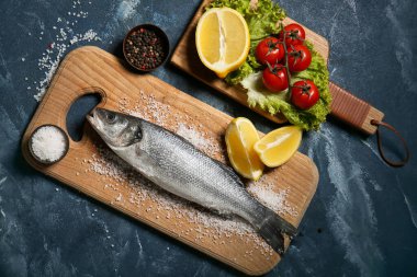 Taze pişmemiş levrek, limon ve domatesli ahşap tahta tahta.