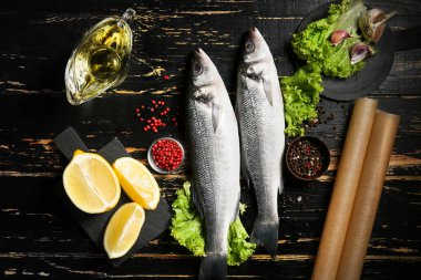 Taze pişmemiş levrek balığı, limon ve baharatlar siyah ahşap arka planda.