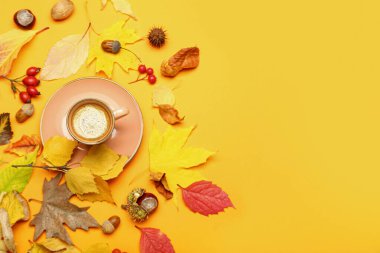 Sarı arka planda bir fincan kahve ve sonbahar yapraklı kompozisyon