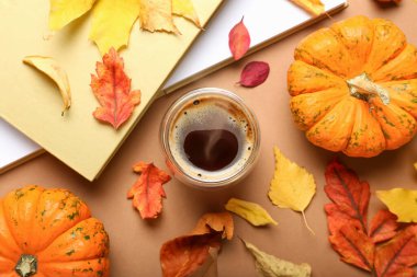 Kahverengi arka planda bir fincan kahve, balkabağı ve sonbahar yapraklı kompozisyon