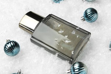 Bir şişe parfüm ve karlı arka planda Noel topları, yakın plan.
