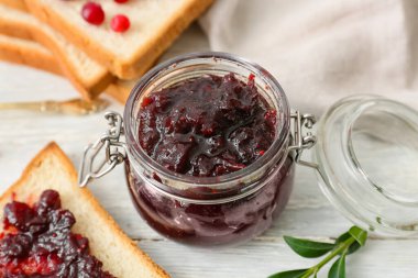 Lezzetli bir kavanoz yaban mersini reçeli ve beyaz ahşap arka planda tost.