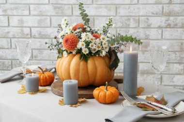 Tuğla duvarın yanındaki masada sunulan balkabağında güzel bir buket sonbahar çiçeği.