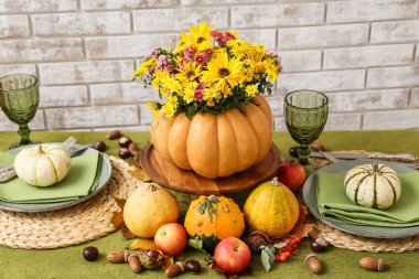 Tuğla duvarın yanındaki masada sunulan balkabağında güzel bir buket sonbahar çiçeği.