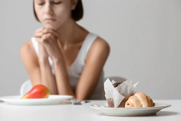 在灰暗的背景下坐在桌旁的年轻女人 专注于食物 厌食症概念 — 图库照片