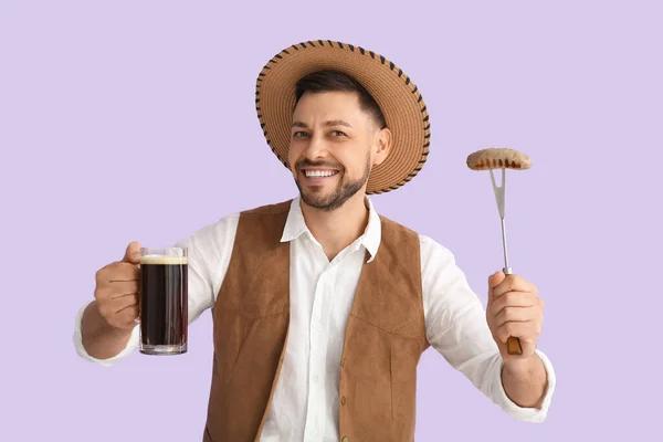 Young man in traditional German clothes with beer and sausage on lilac background