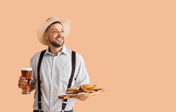 Young man in traditional German clothes with beer and food on beige background