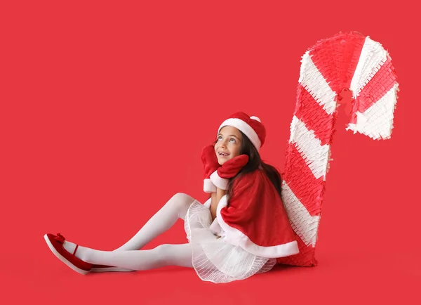 Kleines Mädchen Mit Weihnachtsmütze Und Zuckerstange Pinata Auf Farbigem Hintergrund — Stockfoto