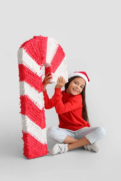 Kleines Mädchen Mit Weihnachtsmütze Und Zuckerrohr Pinata Auf Hellem Hintergrund — Stockfoto