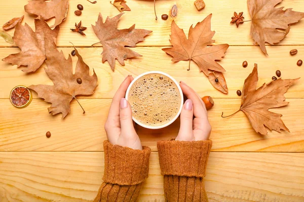 Female hands with cup of coffee and leaves on wooden background