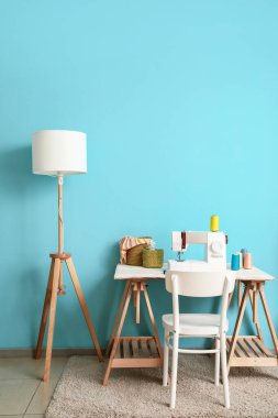 Dikiş makinesi ve lambası mavi duvarın yanında olan terzi işyeri.