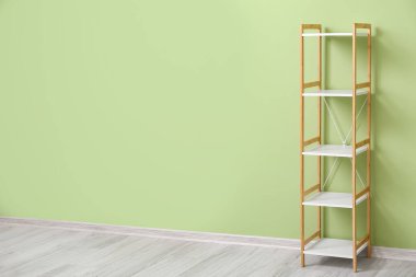 Yeşil duvarın yanında ahşap bir raf var.
