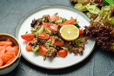 Somonlu lezzetli salata ve koyu arkaplanda taze sebzeler.