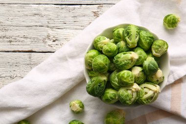 Hafif ahşap zemin üzerinde taze Brüksel lahanası olan bir kase.