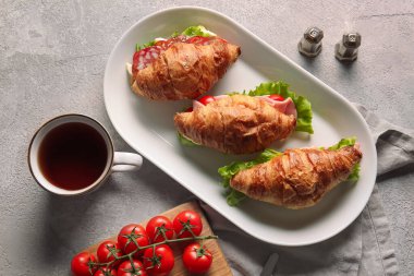 Lezzetli kruvasan sandviçli tabak ve gri arka planda bir fincan içecek.