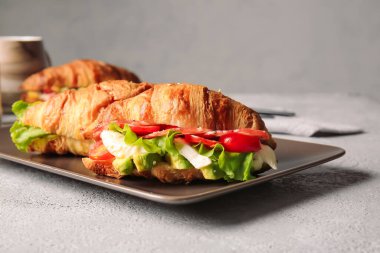 Gri arka planda lezzetli kruvasan sandviçli tabak.