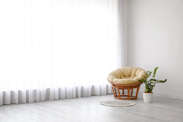 Armchair and houseplant near big window with light curtains