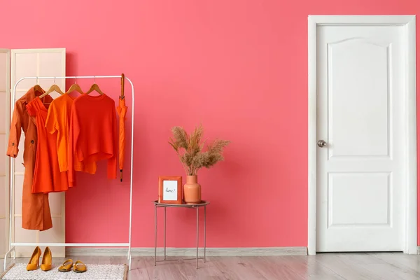 Interior of stylish hallway with bright red clothes and pink wall