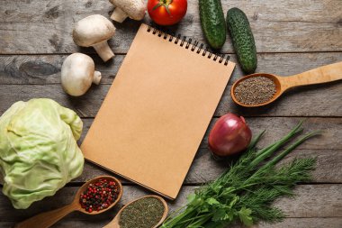 Tarif kitabı, sebzeler ve ahşap arka planda farklı baharatlar bulunan katı kaşıklar.