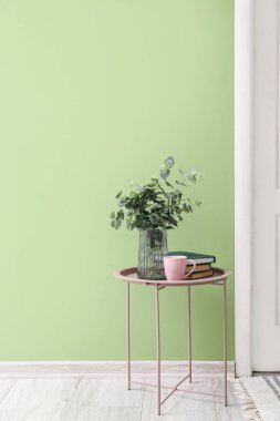 Okaliptüs dallı vazo, bir fincan çay ve renkli duvarın yanındaki masada kitaplar.