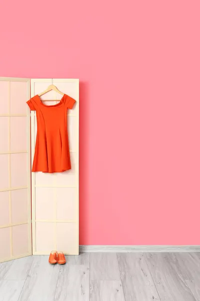 Light folding screen with red dress and shoes near pink wall