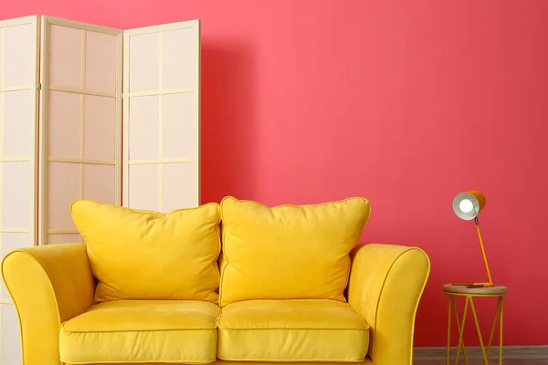 Yellow sofa, table with lamp and folding screen near pink wall