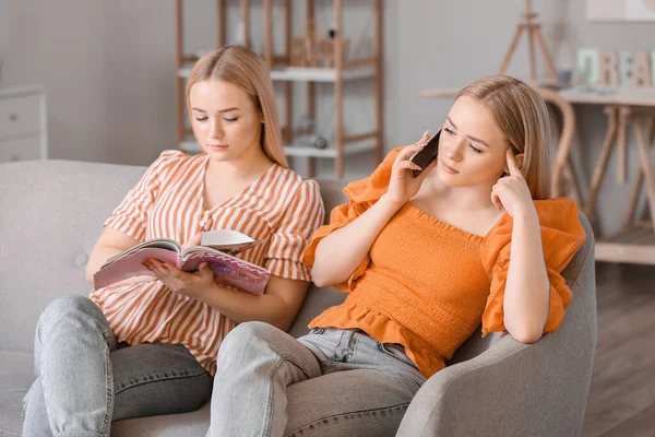 Young Twin Sisters Reading Magazine Talking Mobile Phone Home — Stock Photo, Image