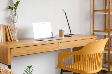 Modern laptop, kağıt bardak kahve ve lamba beyaz duvarın yanındaki ahşap masada.