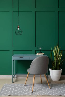 Rahat işyeri ve yeşil duvarın yanındaki ev bitkisi olan bir oda.