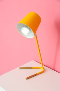 Pembe duvarın yanındaki rafta parlayan sarı lamba.