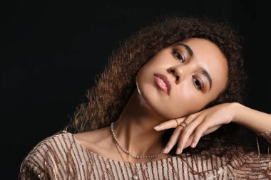 Siyah arka planda şık mücevherleri olan şık bir Afro-Amerikan kadın.