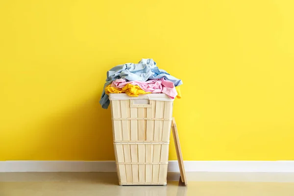 黄色の壁の近くに洗濯付きの木製バスケット — ストック写真