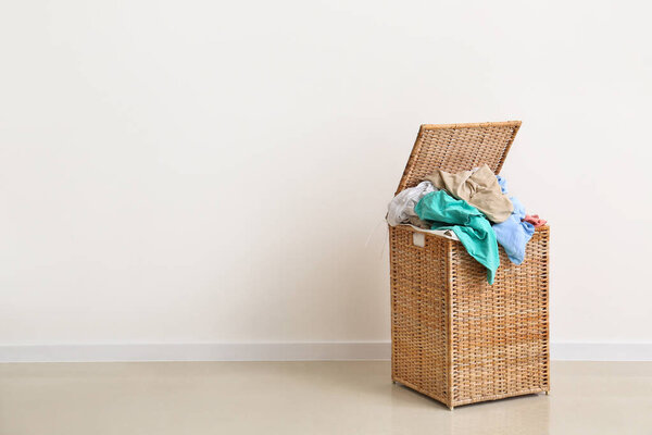 Wicker basket full of dirty clothes near light wall