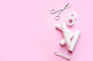 Cerrahi makas, tıbbi alçı, bandaj ruloları ve renk arka planında pamuk tomurcukları.