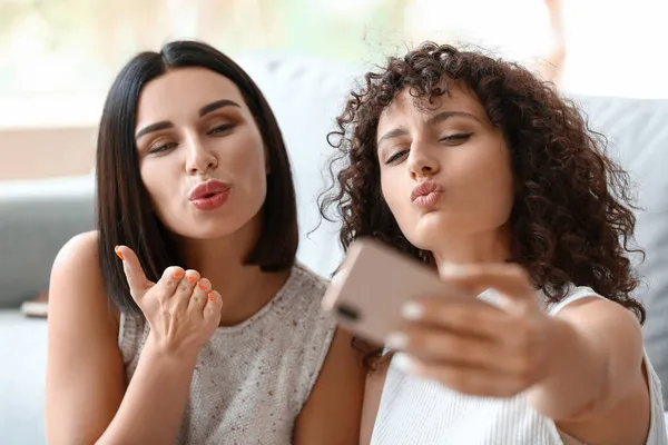 Young sisters giving air kiss and taking selfie in room