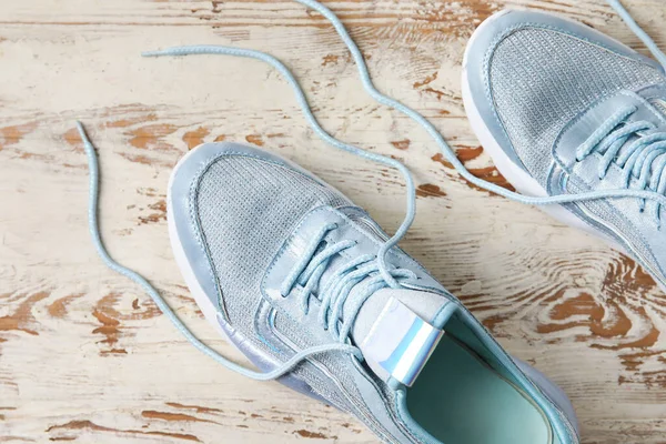 Pair of sportive shoes with untied laces on light wooden background, closeup