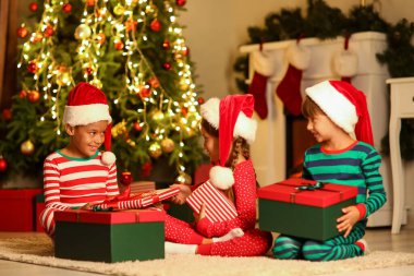 Noel Baba şapkalı küçük çocuklar ve evde Noel hediyeleri.