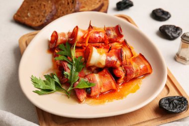 Gevrek domuz pastırmasında pişirilmiş lezzetli kuru erikli tabak, ahşap tahtada sos ve maydanoz, yakın plan.