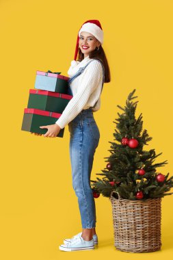 Sarı arka planda hediyeleri ve Noel ağacı olan genç bir kadın.