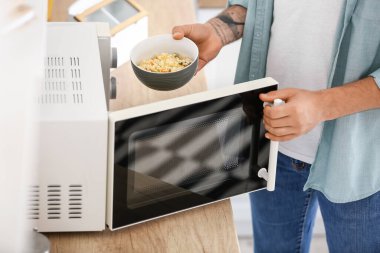 Genç adam pirinçle kaseyi mikrodalga fırına koyuyor.