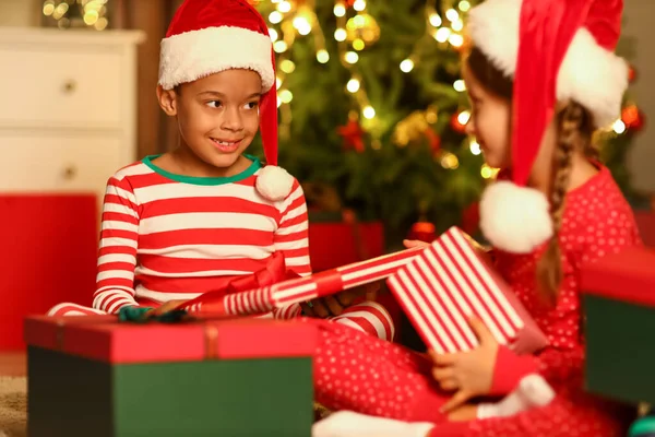 戴着圣诞礼帽的小孩带着圣诞礼物在家里 — 图库照片