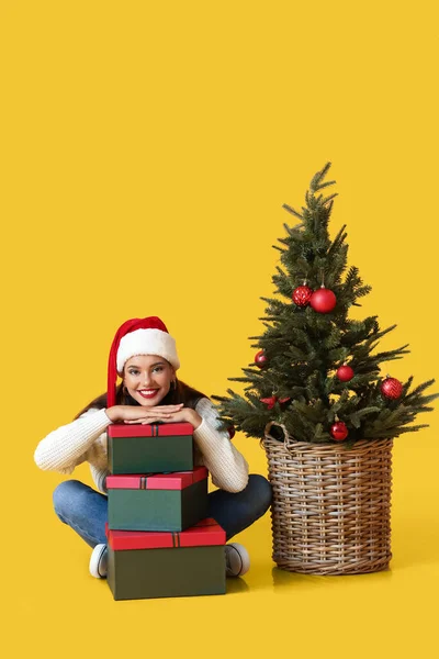 若いです女性とともにギフトとクリスマスツリー上の黄色の背景 — ストック写真