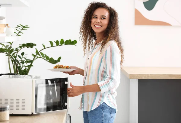 Genç Afro Amerikalı Kadın Mutfakta Mikrodalga Fırına Yemek Koyuyor — Stok fotoğraf