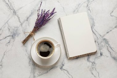 Bir fincan kahve, boş defter ve arka planda lavanta çiçekleri.