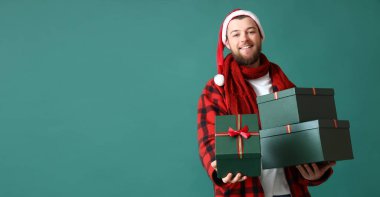 Noel Baba şapkalı mutlu bir adam elinde yeşil arka planda hediye kutuları ve mesaj için yeri var.